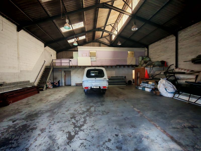 Spacious industrial warehouse featuring high ceilings with exposed steel trusses, a mezzanine level, concrete flooring, and natural light provided by integrated skylights.
