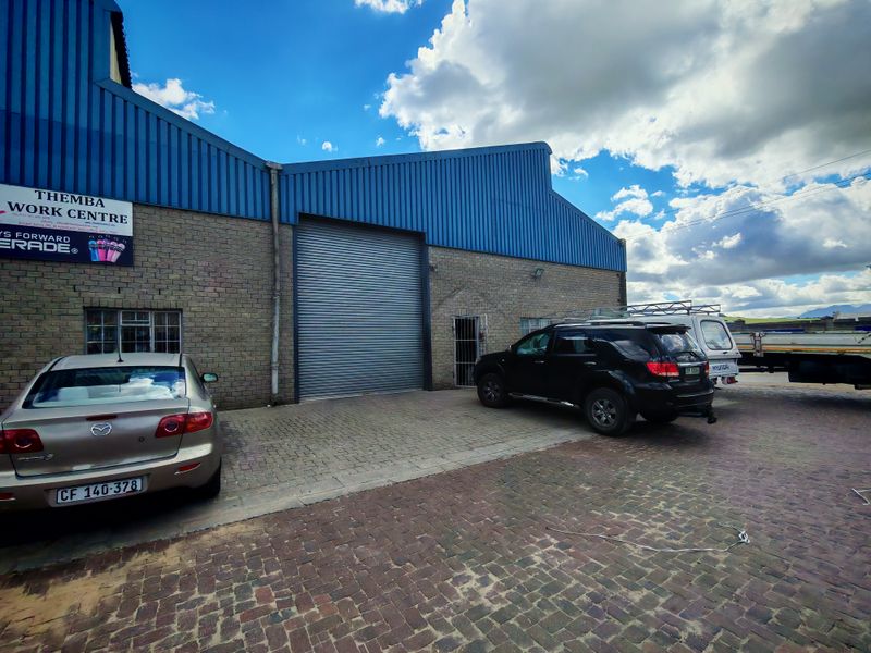 Front elevation of an industrial warehouse featuring a large roller shutter door, brick construction, and paved exterior parking area.