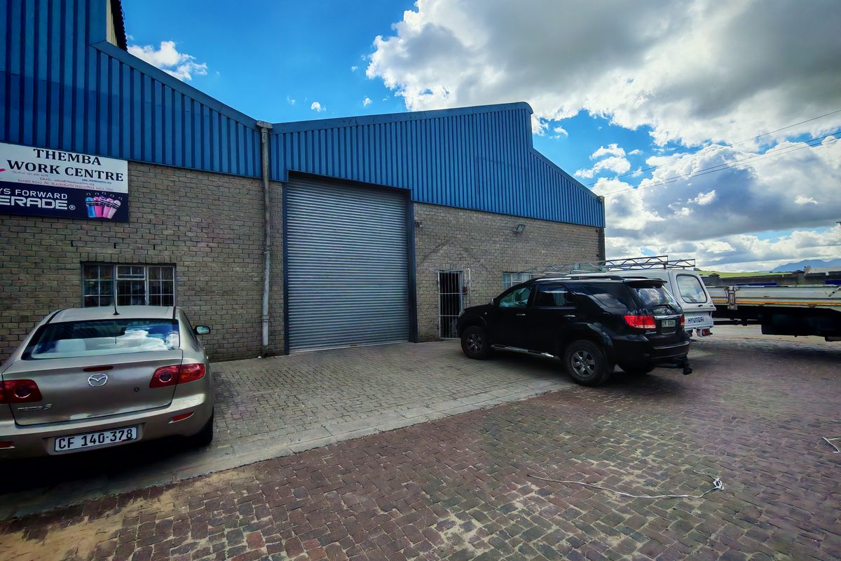 Front elevation of an industrial warehouse featuring a large roller shutter door, brick construction, and paved exterior parking area.