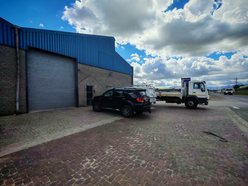 Industrial property exterior featuring a large roller shutter door, brick and metal cladding construction, and a paved driveway area.
