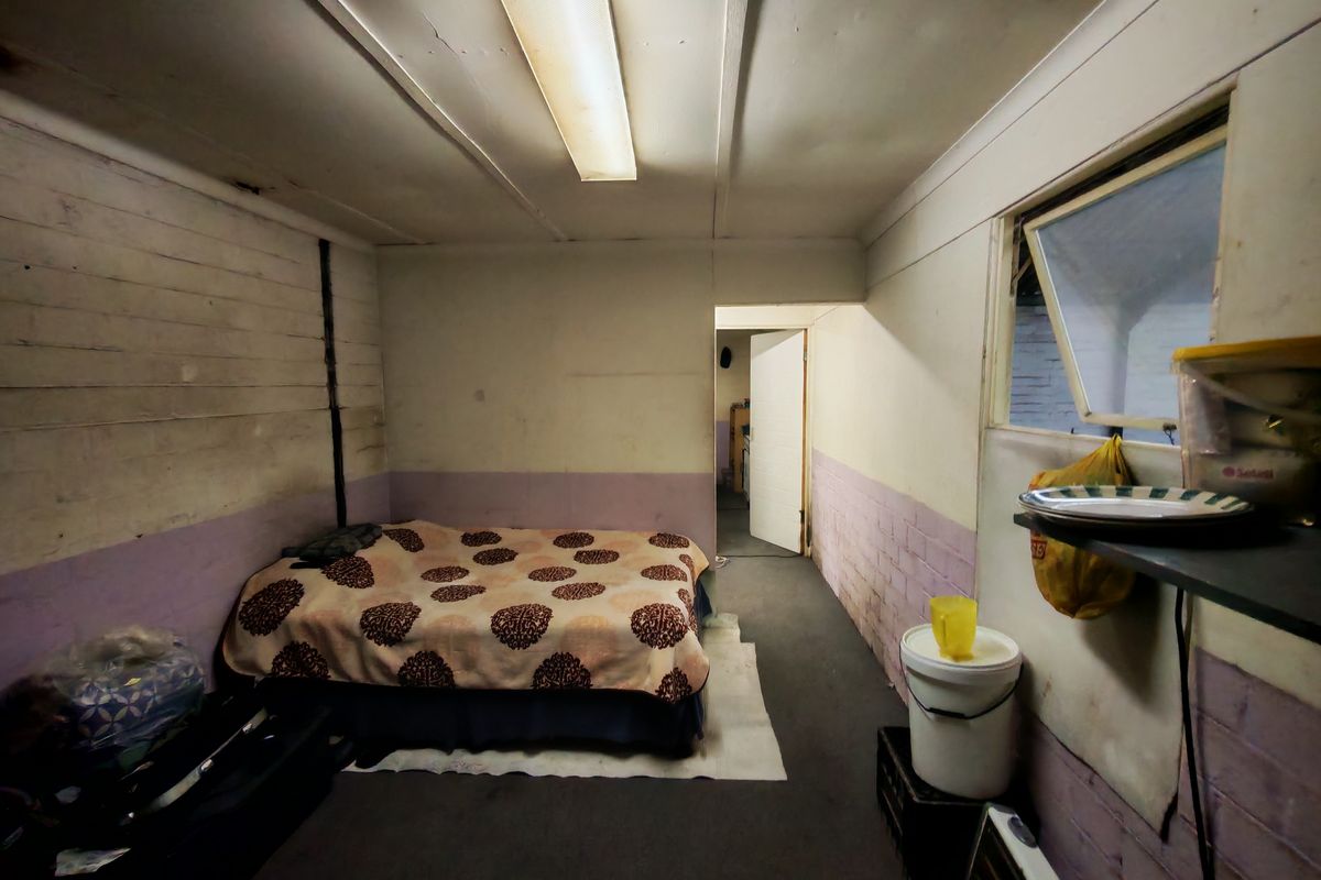 A basic bedroom space featuring painted brick walls, an awning window, and a fluorescent ceiling light, requiring cosmetic updates and refurbishment.