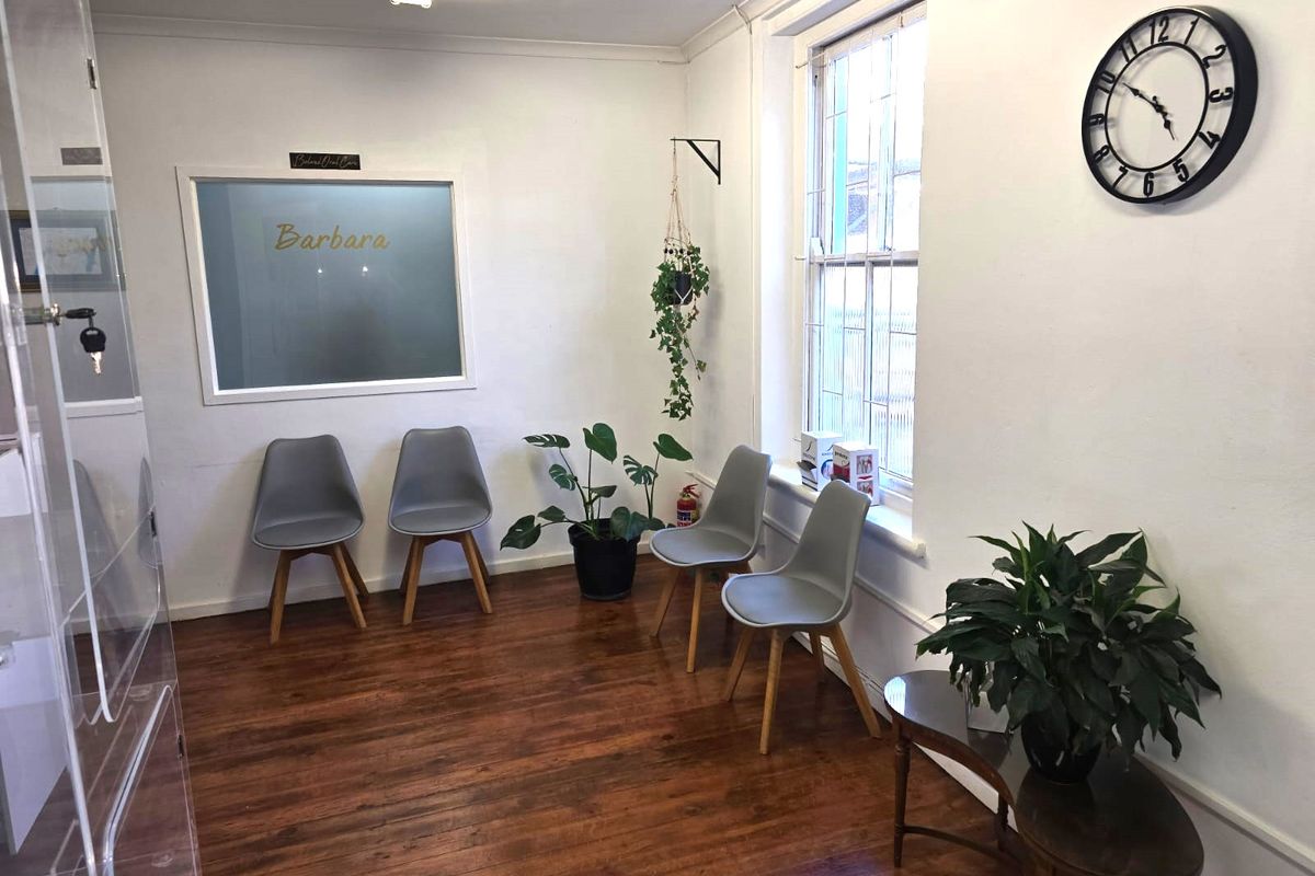 A professional office or reception area featuring timber flooring, a large sash window, and an internal glass partition.