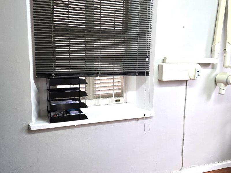A functional office or clinical space featuring laminate flooring, venetian blinds, and wall-mounted equipment infrastructure.