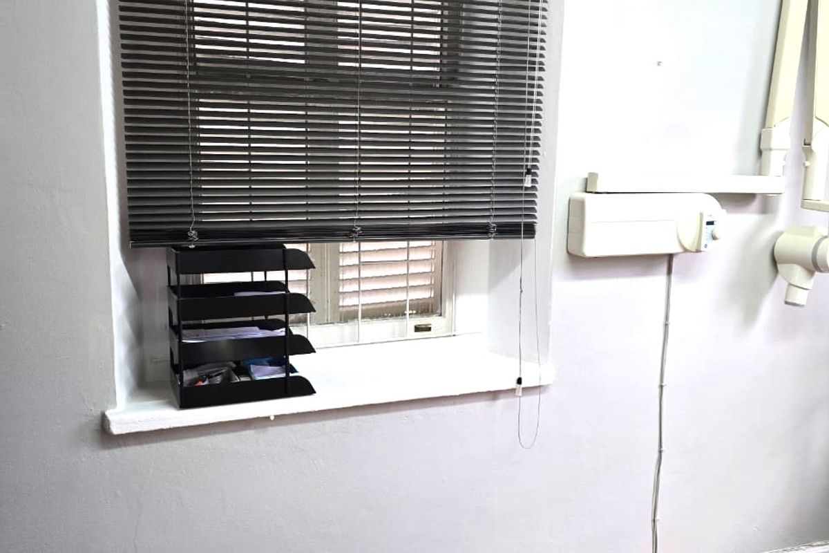A functional office or clinical space featuring laminate flooring, venetian blinds, and wall-mounted equipment infrastructure.