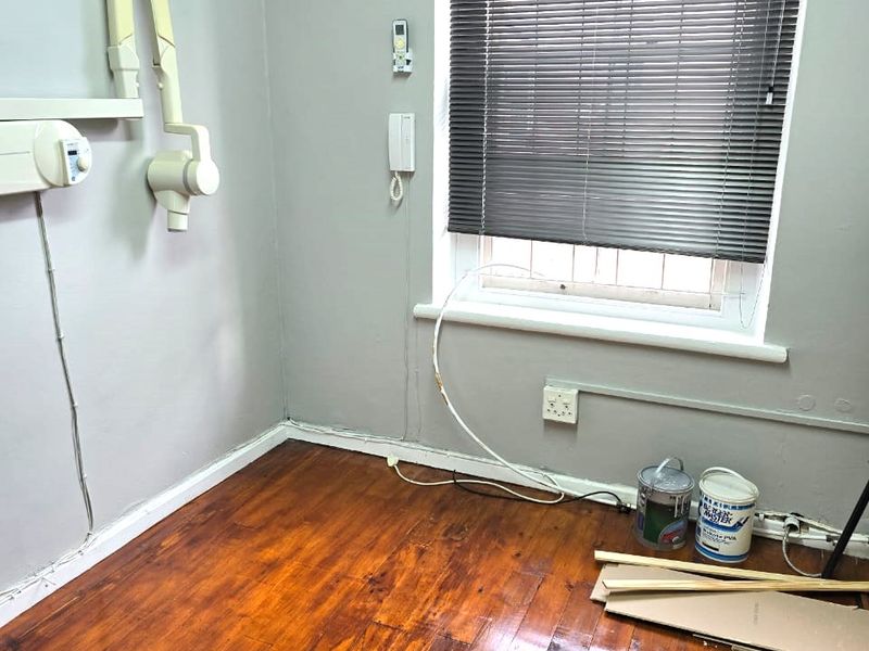 A vacant commercial office space featuring hardwood flooring, a wall-mounted air conditioning unit, and a dental x-ray arm, suitable for medical or professional use.