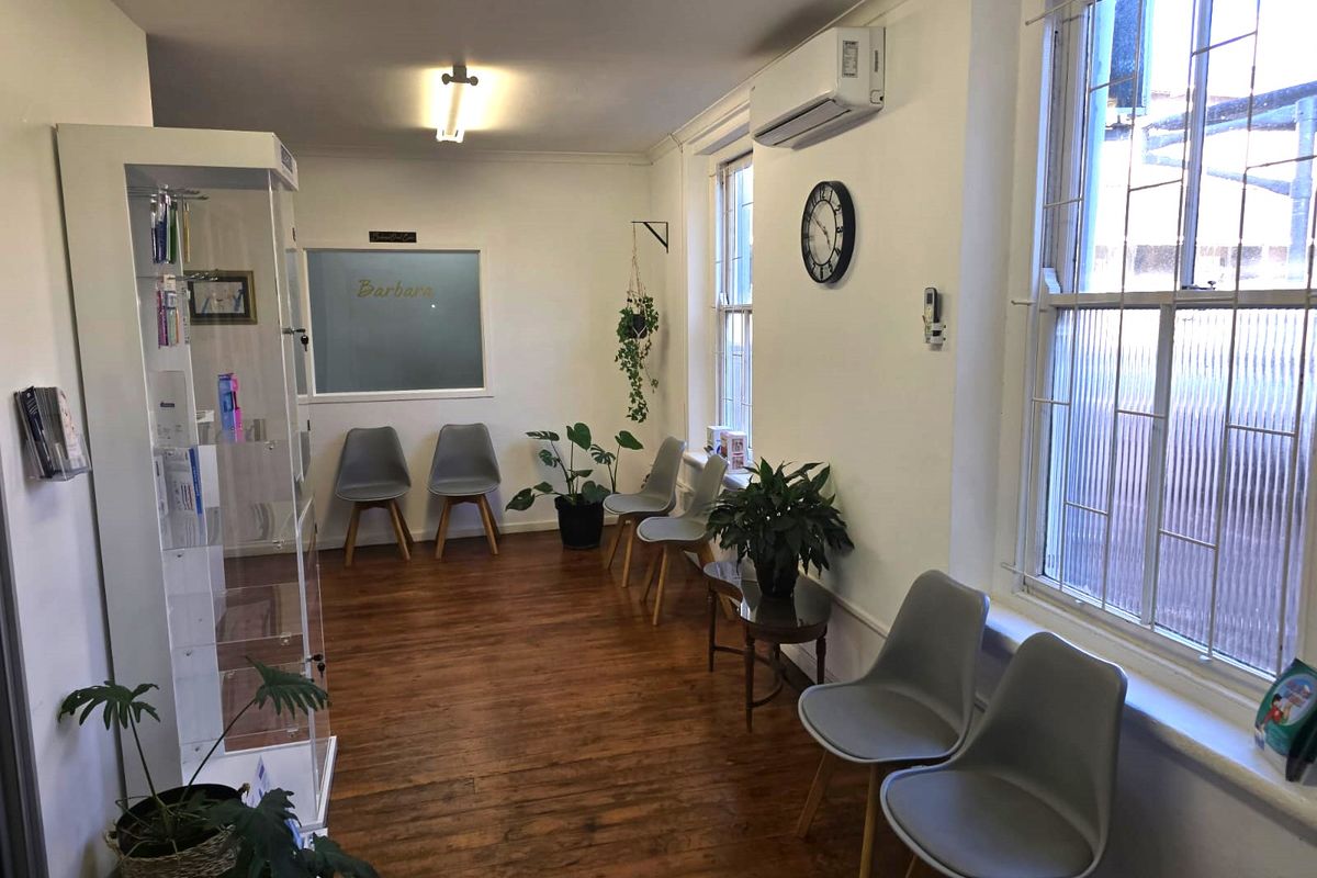 A well-maintained commercial waiting area featuring polished timber flooring, split system air conditioning, and large sash windows with security bars.