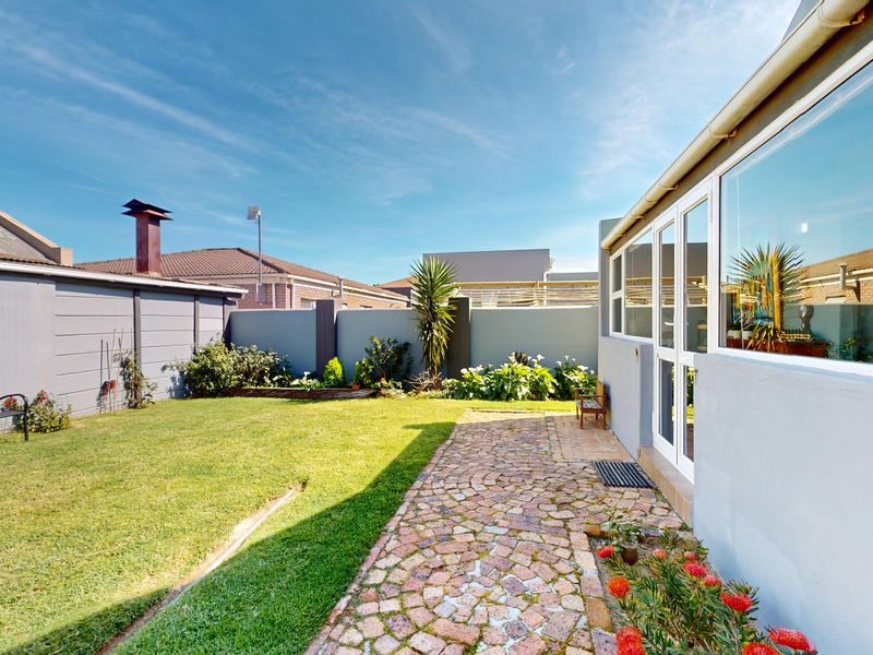A well-maintained rear garden featuring a paved walkway, lawn area, and boundary walls, providing direct access to the home through sliding glass doors.