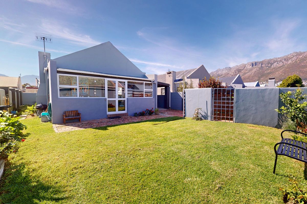 Rear view of the property featuring a well-maintained lawn, brick paved patio area, and secure boundary walls with mountain views in the background.