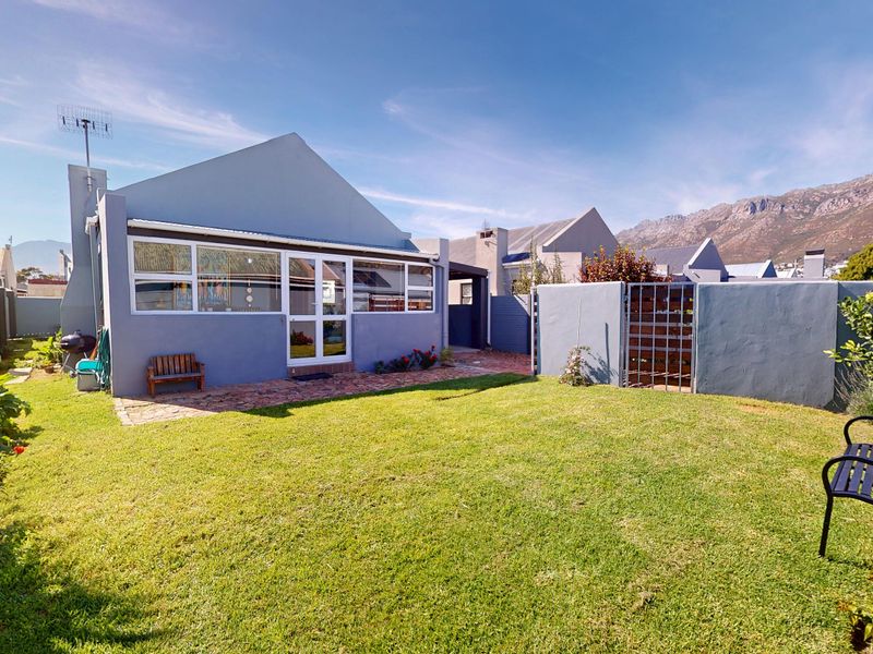 Rear view of the property featuring a well-maintained lawn, brick paved patio area, and secure boundary walls with mountain views in the background.