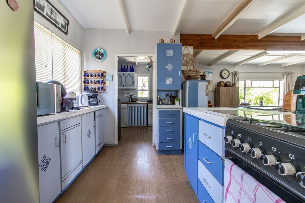 A functional kitchen featuring blue cabinetry, laminate countertops, a built-in stove, and an adjacent scullery area with exposed ceiling beams.