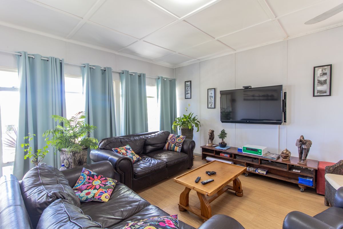 A comfortable living room featuring wood-look flooring, a panelled ceiling, and large windows that provide ample natural light.