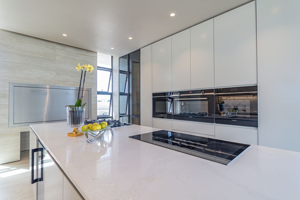Modern kitchen featuring a large stone-topped island with an integrated induction cooktop, sleek handleless cabinetry, and high-end built-in ovens.