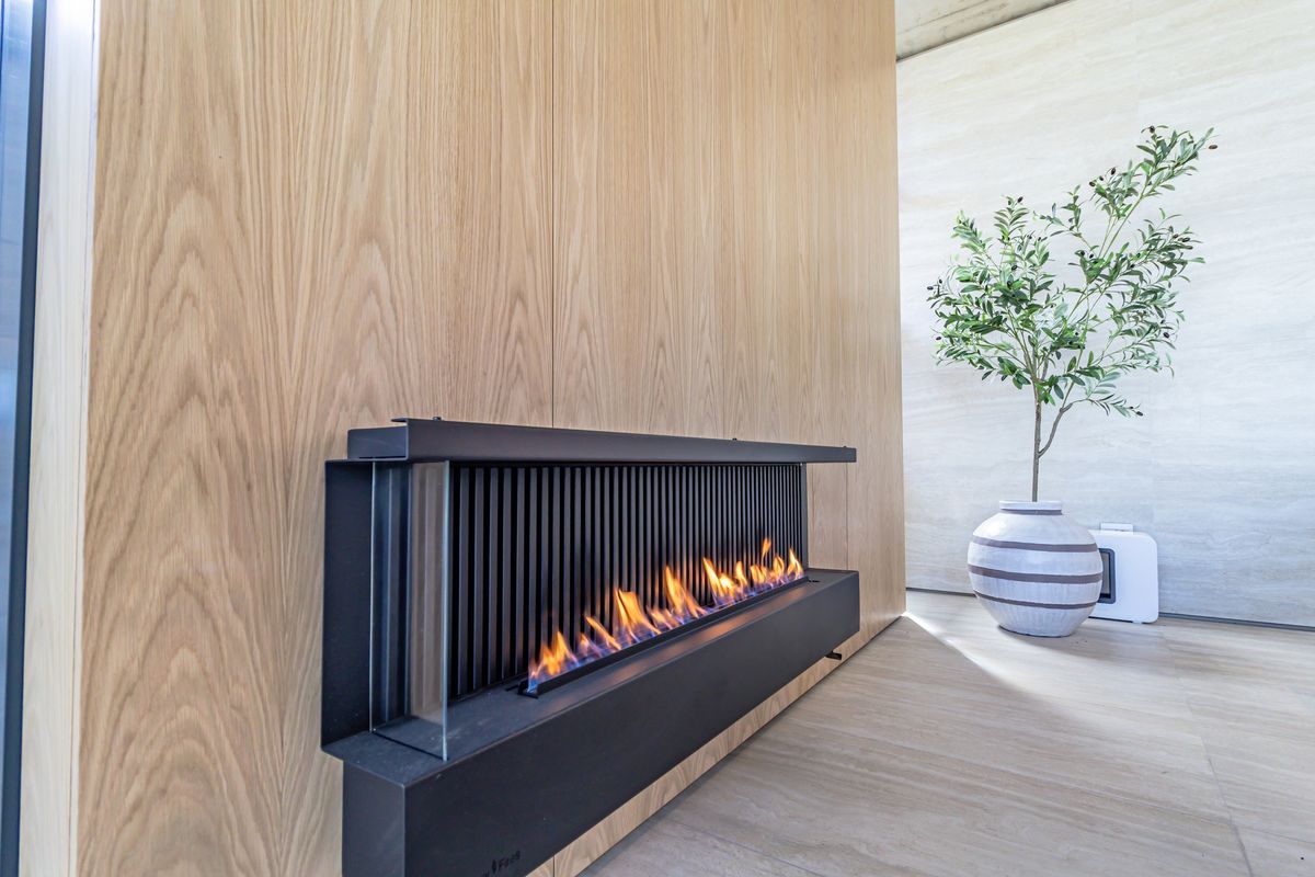 A modern, sleek linear fireplace integrated into a light wood-paneled feature wall, creating a sophisticated focal point in the living space.