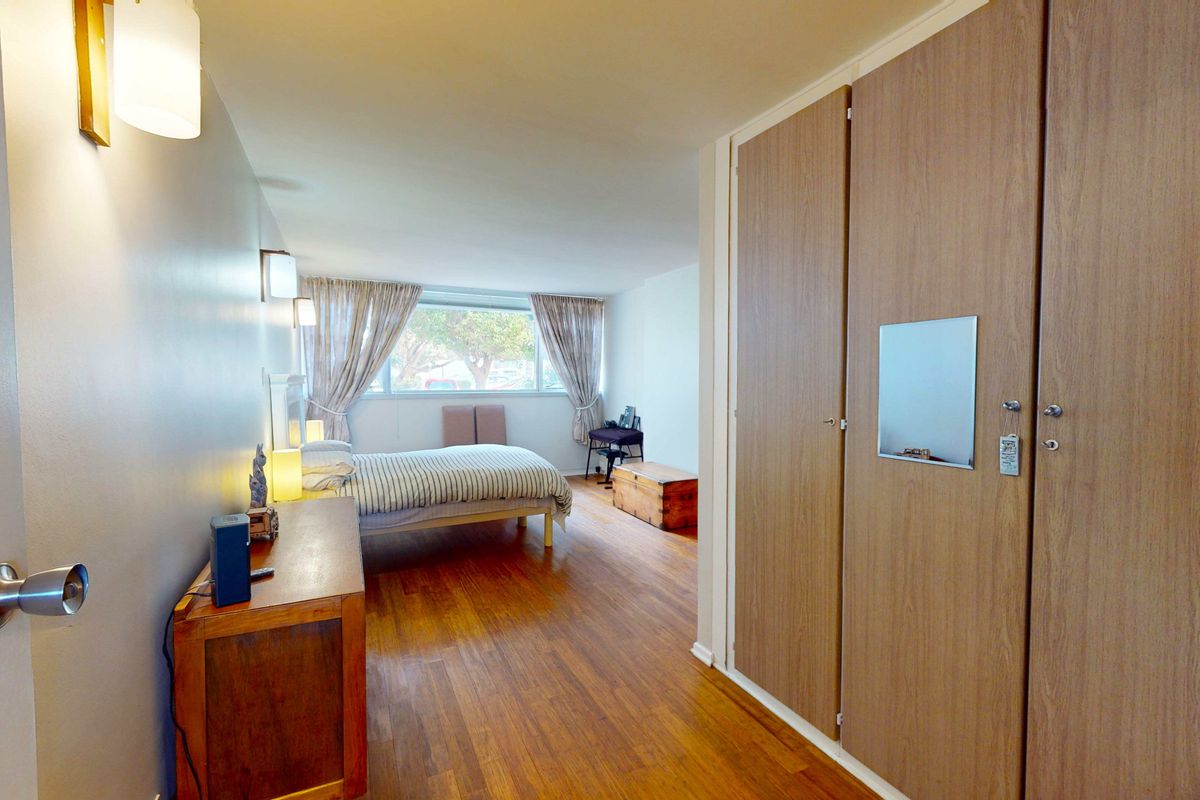 A spacious bedroom featuring warm-toned wood flooring, built-in wooden cabinetry, and large windows that provide natural light.