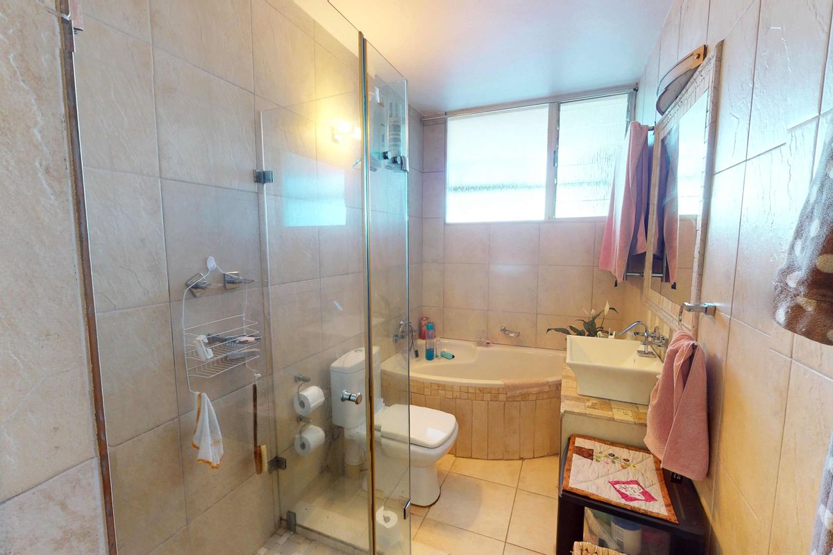 A functional bathroom featuring a glass-enclosed shower, a built-in bathtub, a vanity basin, and neutral wall and floor tiling.