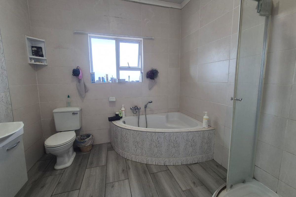 A functional bathroom featuring a corner bathtub, separate shower enclosure, toilet, and vanity, finished with neutral wall tiles and wood-look floor tiles.
