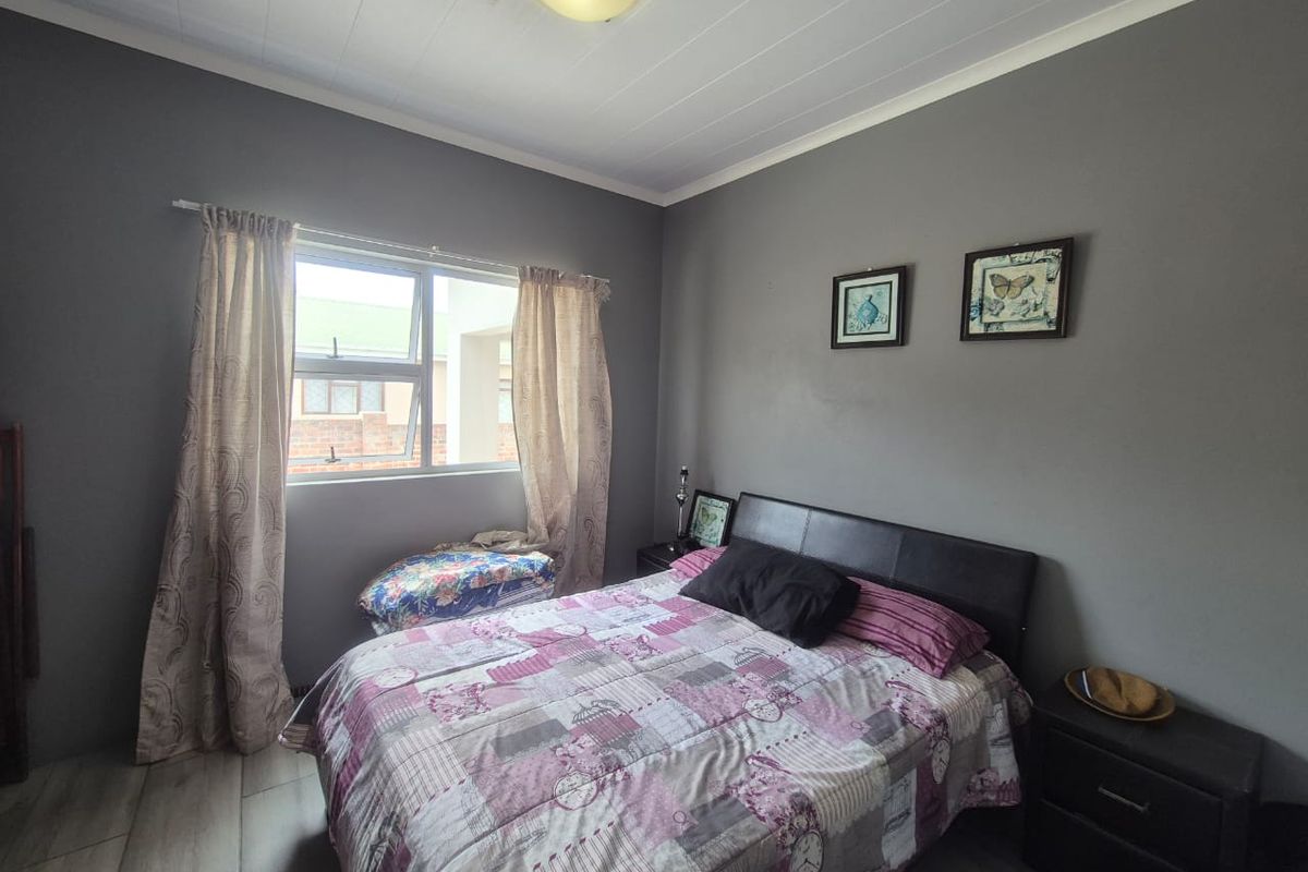A bedroom featuring grey painted walls, wood-look flooring, and a window with natural light.