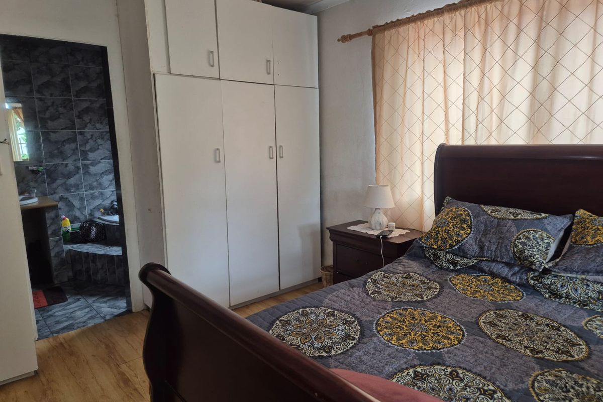 Bedroom featuring built-in white cabinetry and laminate flooring, with an adjoining en-suite bathroom visible through the doorway.