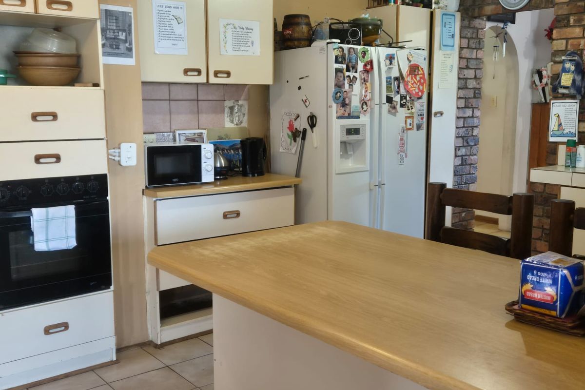 A dated kitchen featuring built-in cabinetry, an integrated oven, and a central island bench, with a brick feature wall leading to an adjacent space.