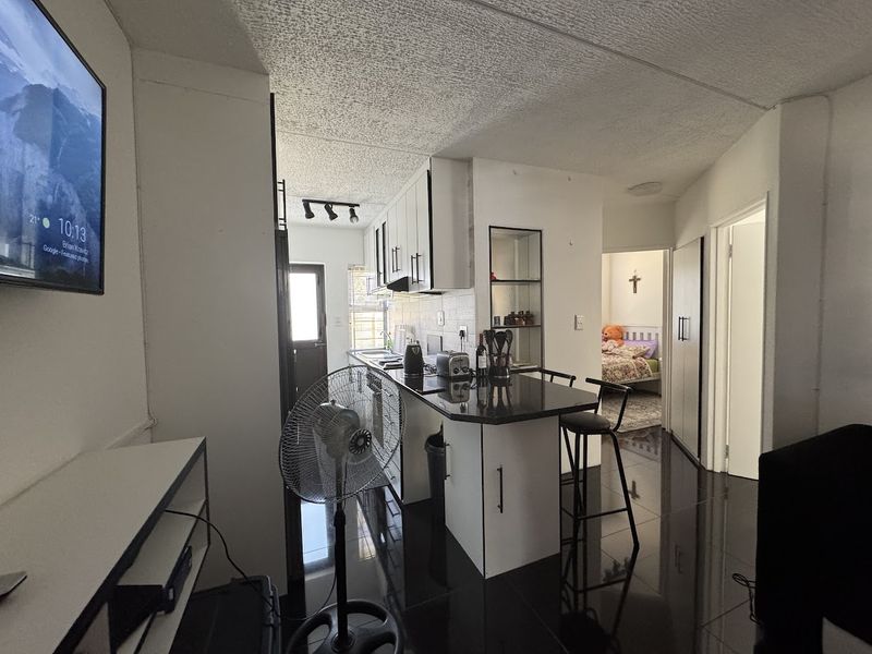 Open plan kitchen and living area featuring dark tiled flooring, white cabinetry, granite countertops, and a breakfast bar, leading to adjacent bedroom and hallway.