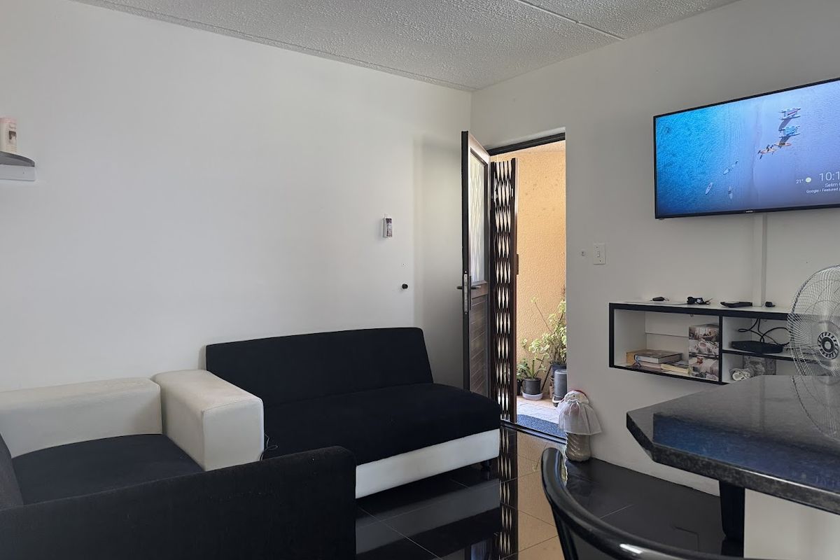 A compact living area featuring dark tiled flooring, built-in shelving, and direct access to an outdoor space through a security gate.