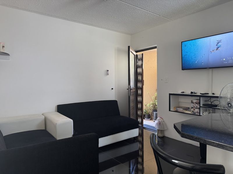 A compact living area featuring dark tiled flooring, built-in shelving, and direct access to an outdoor space through a security gate.