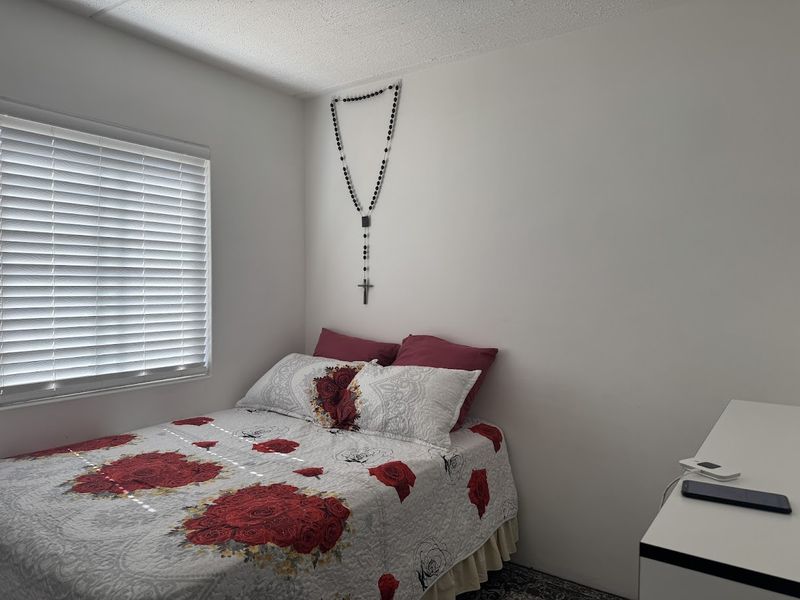 A simple bedroom featuring a window with venetian blinds and neutral wall finishes.