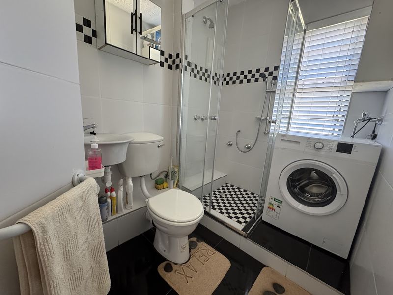 Compact bathroom featuring a shower enclosure, pedestal basin, toilet, and an integrated washing machine with a classic black and white tiled aesthetic.