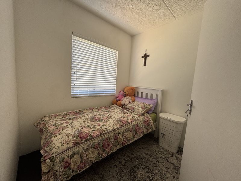 A compact bedroom featuring a window with venetian blinds and a textured ceiling finish.