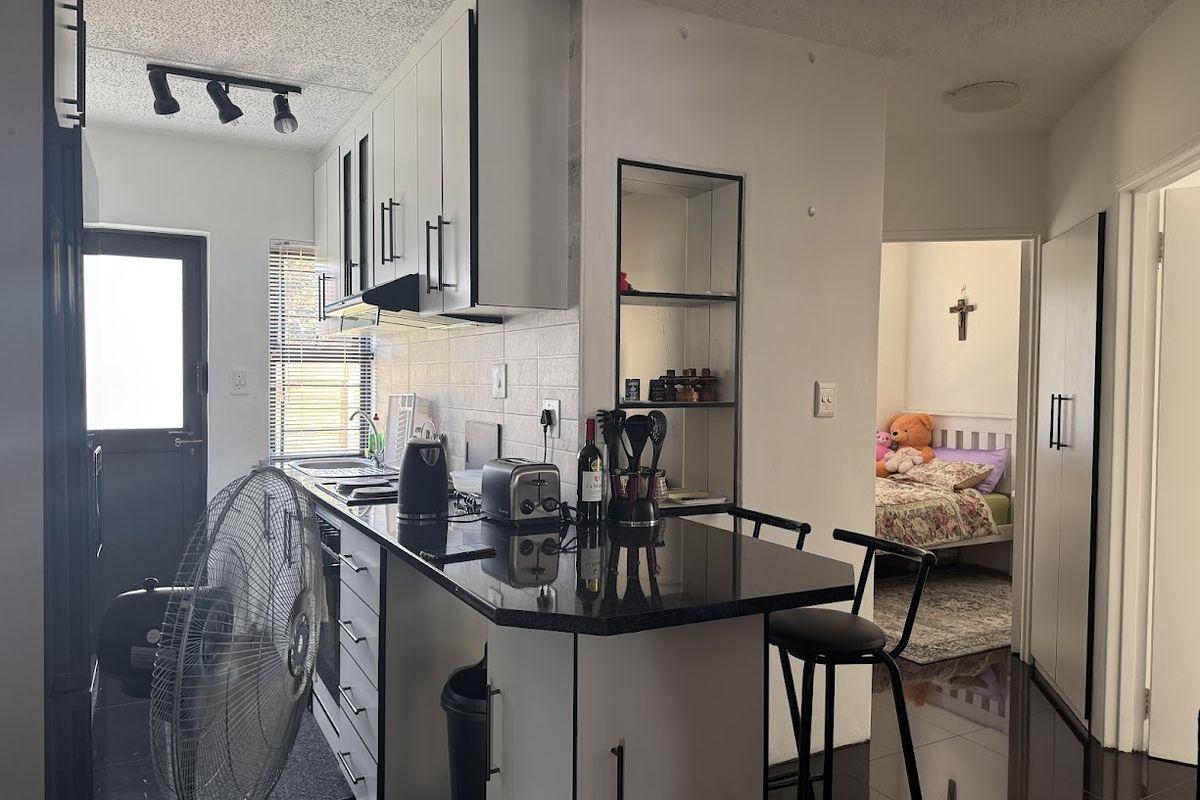 Modern kitchen featuring white cabinetry, black granite countertops, tiled backsplash, and integrated track lighting, with a view into an adjacent bedroom.