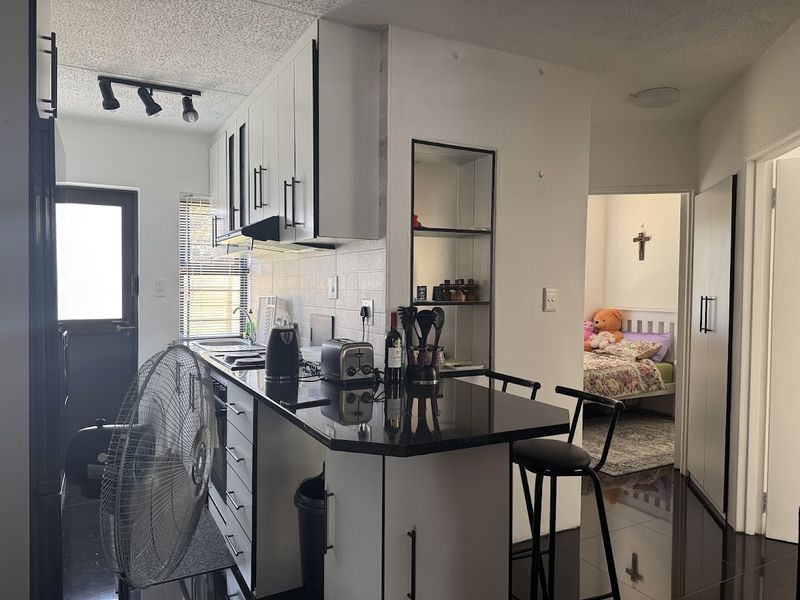 Modern kitchen featuring white cabinetry, black granite countertops, tiled backsplash, and integrated track lighting, with a view into an adjacent bedroom.