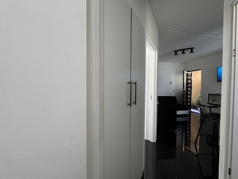 A clean hallway featuring modern built-in cupboards, high-gloss tiled flooring, and track lighting, leading into the main living area.