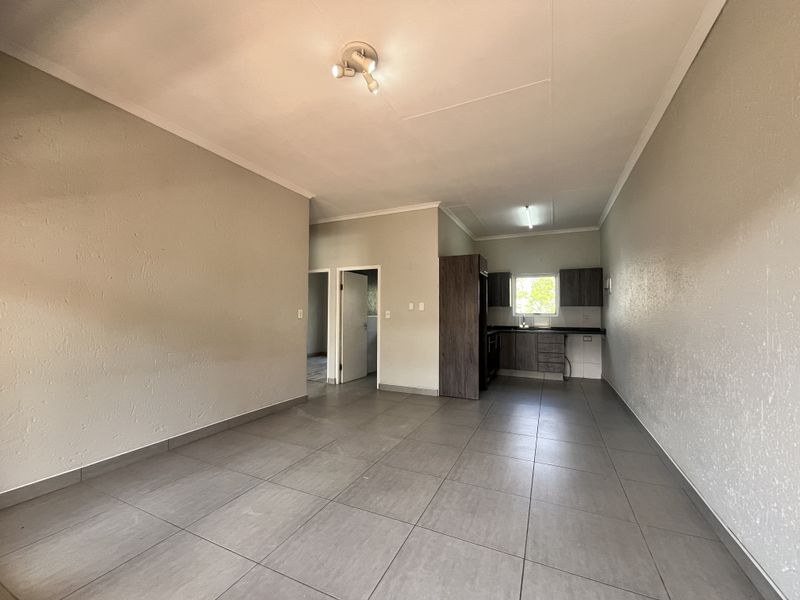An open-plan living and kitchen area featuring neutral tiled flooring, modern cabinetry, and a functional layout, presented in a clean, vacant condition.