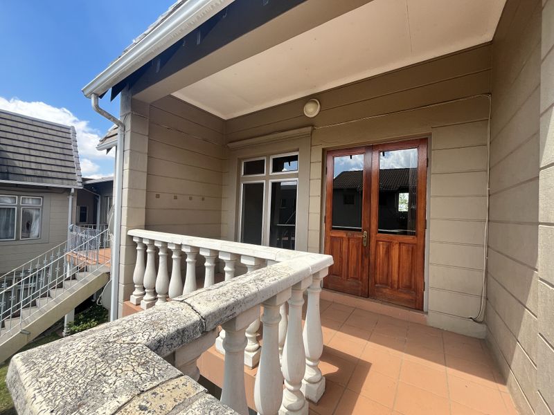 A covered balcony featuring tiled flooring, a classic balustrade, and double wooden doors providing access to the apartment interior.