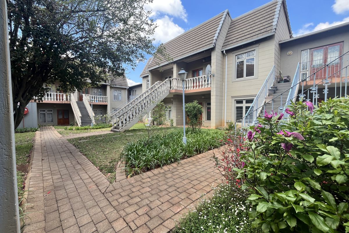 A view of the apartment complex exterior featuring paved walkways, landscaped garden areas, and external staircases leading to upper-level units.