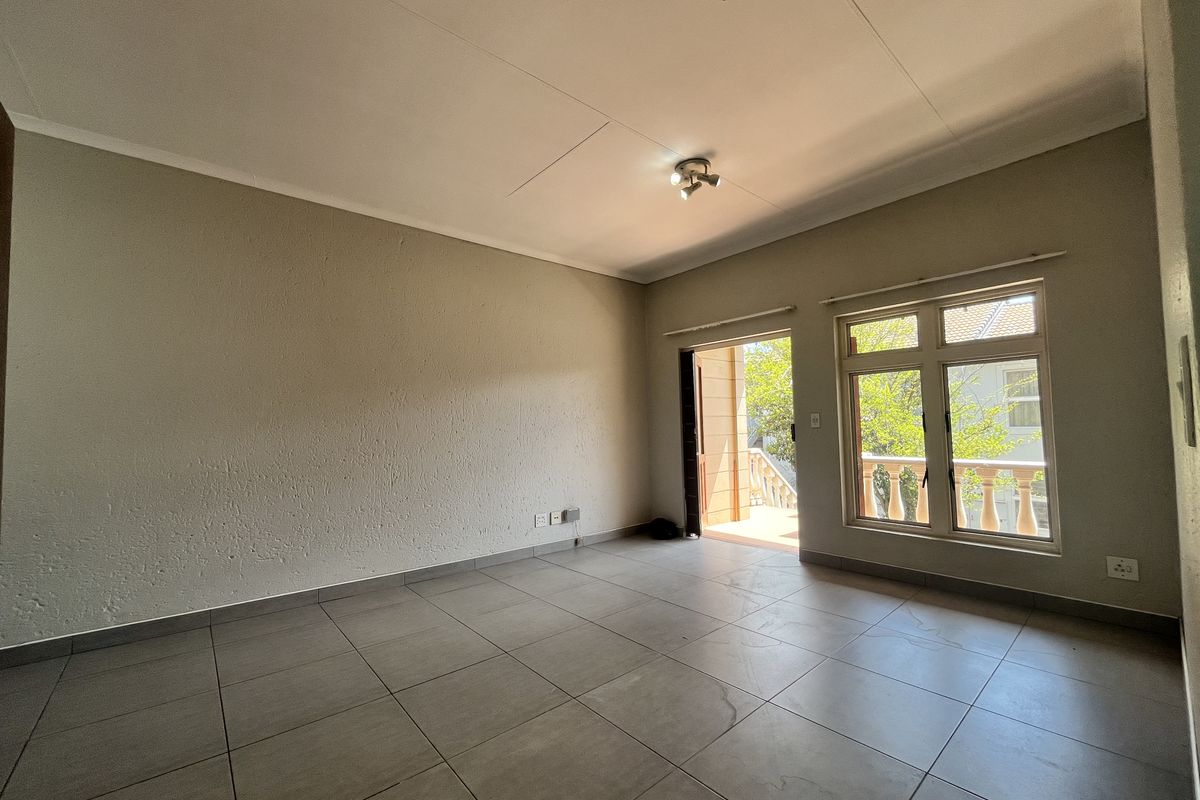 An empty living room featuring neutral tiled flooring, a coved ceiling, and direct access to an outdoor balcony through a sliding glass door.