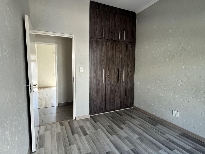 A clean, empty bedroom featuring modern grey laminate flooring, neutral textured walls, and dark wood-finish built-in cupboards.