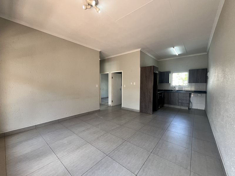 An open-plan living and kitchen area featuring neutral tiled flooring, built-in cabinetry, and direct access to adjacent rooms.