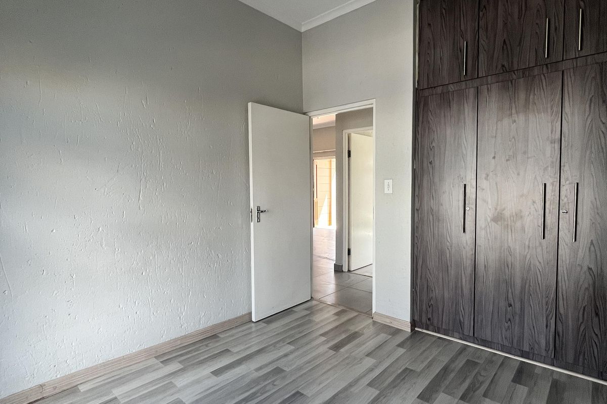 A clean, empty bedroom featuring modern grey laminate flooring and dark wood-finish built-in cupboards, offering a neutral canvas for personalization.