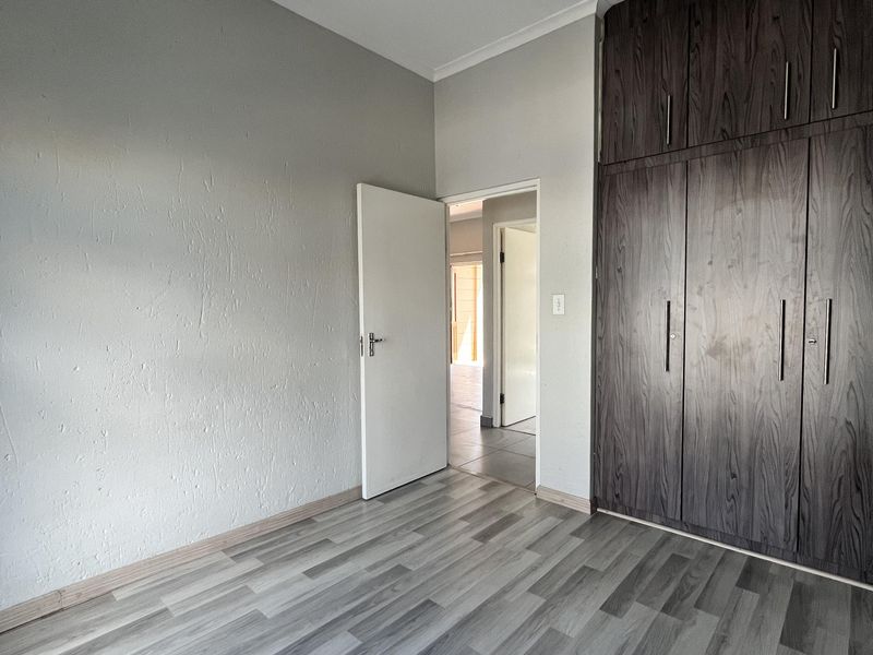 A clean, empty bedroom featuring modern grey laminate flooring and dark wood-finish built-in cupboards, offering a neutral canvas for personalization.