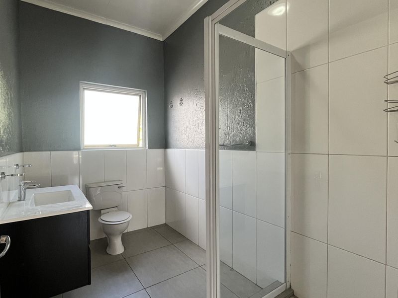 A clean, modern bathroom featuring a vanity with basin, a toilet, and a glass-enclosed shower with tiled walls and flooring.