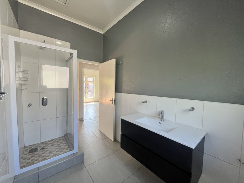 A modern bathroom featuring a glass-enclosed shower, a contemporary vanity with a basin, and neutral wall and floor tiling.