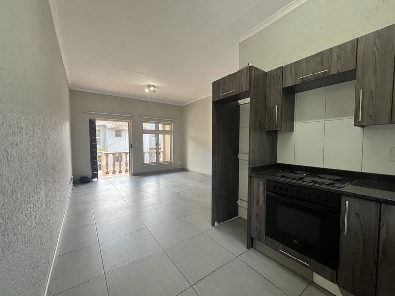 Open-plan living area featuring a modern kitchen with built-in oven and hob, tiled floors, and direct access to a private balcony.