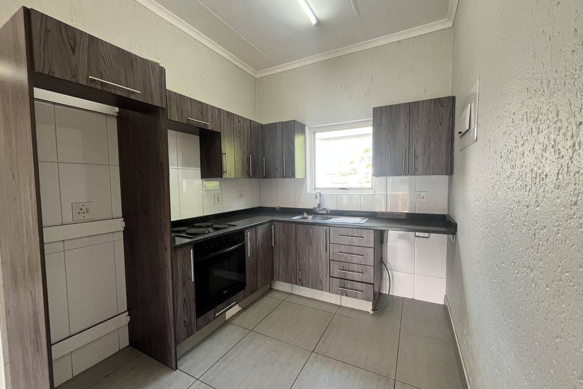 A functional kitchen featuring dark wood-grain cabinetry, laminate countertops, a built-in oven, and tiled flooring, offering a clean and practical workspace.