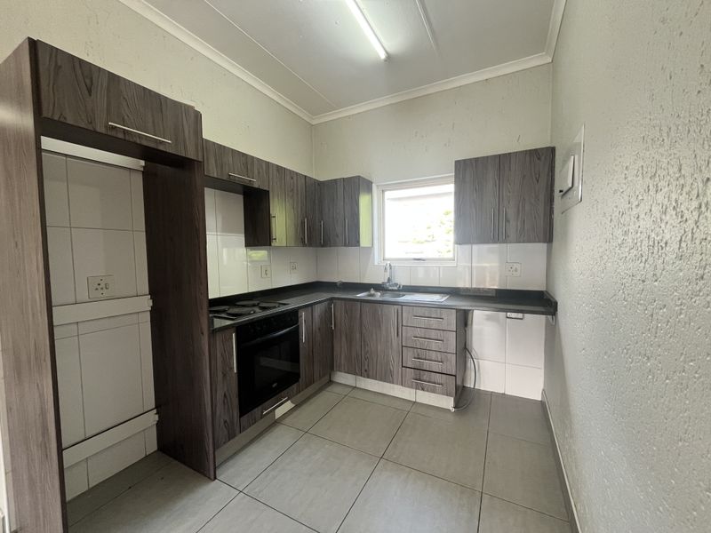 A functional kitchen featuring dark wood-grain cabinetry, laminate countertops, a built-in oven, and tiled flooring, offering a clean and practical workspace.