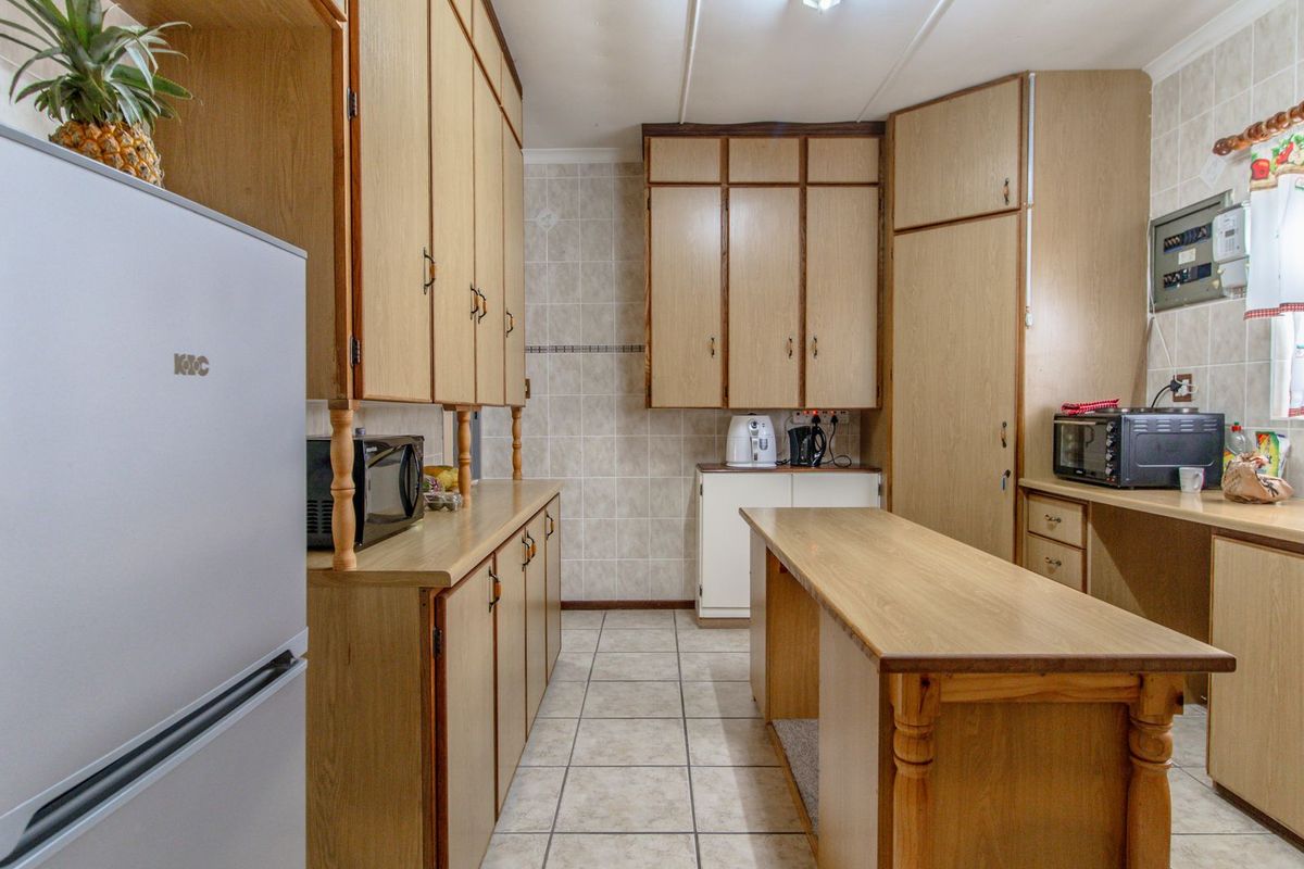 A functional kitchen featuring extensive wood-look cabinetry, tiled flooring, and a central island, offering ample storage and workspace for daily meal preparation.