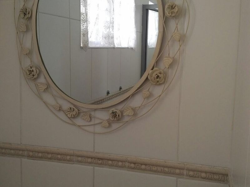 A bathroom featuring white wall tiles with a decorative border and a wall-mounted mirror.
