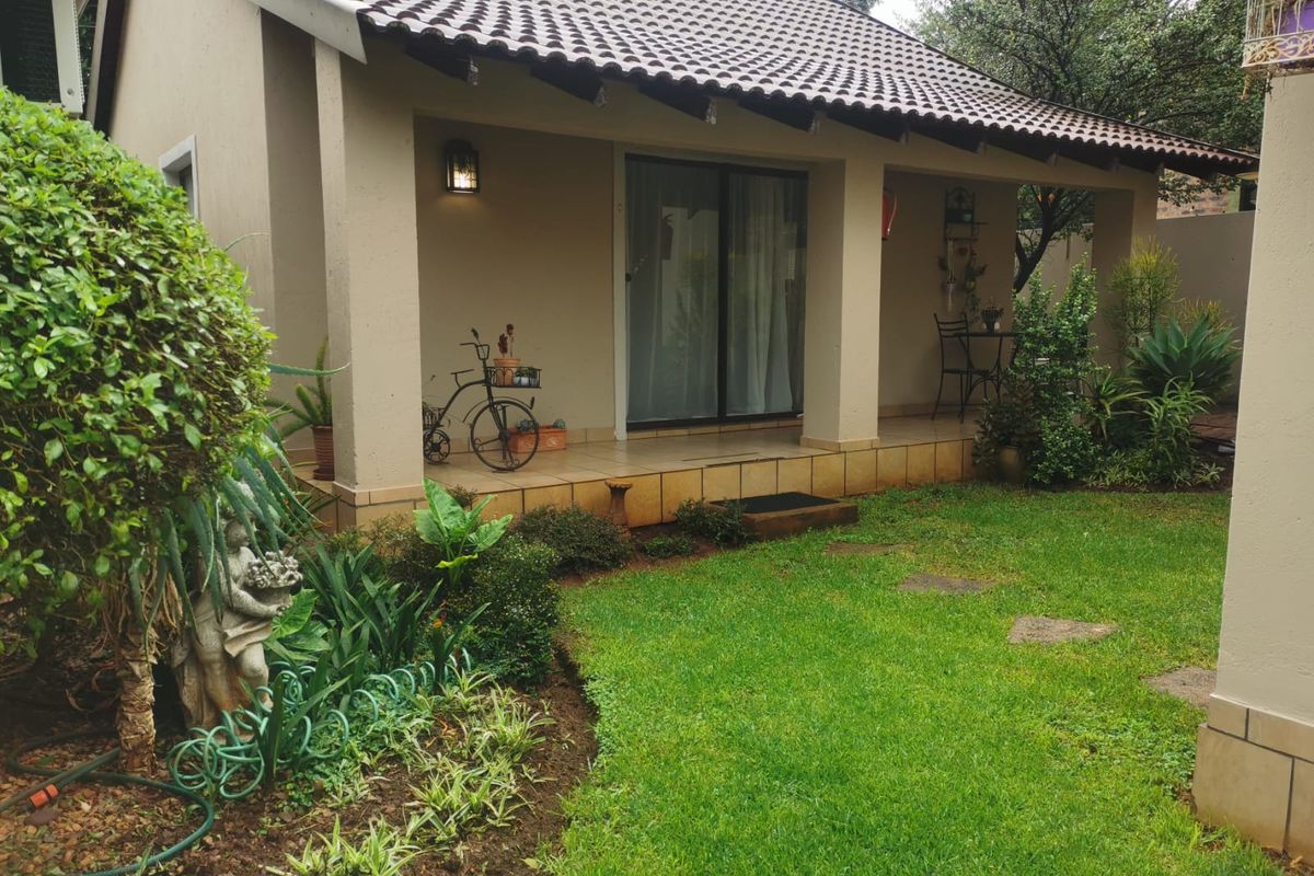 A covered patio area with tiled flooring and sliding glass doors, overlooking a well-maintained private garden space.