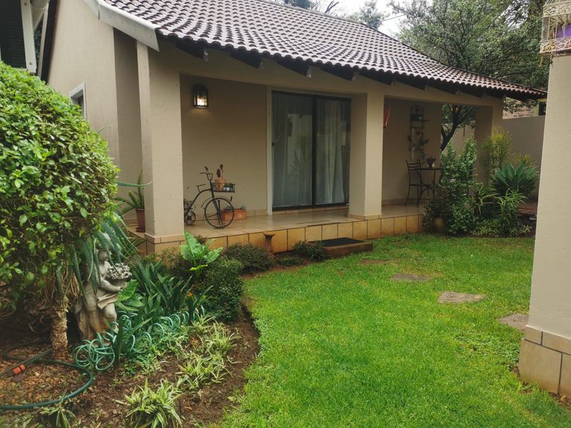 A covered patio area with tiled flooring and sliding glass doors, overlooking a well-maintained private garden space.
