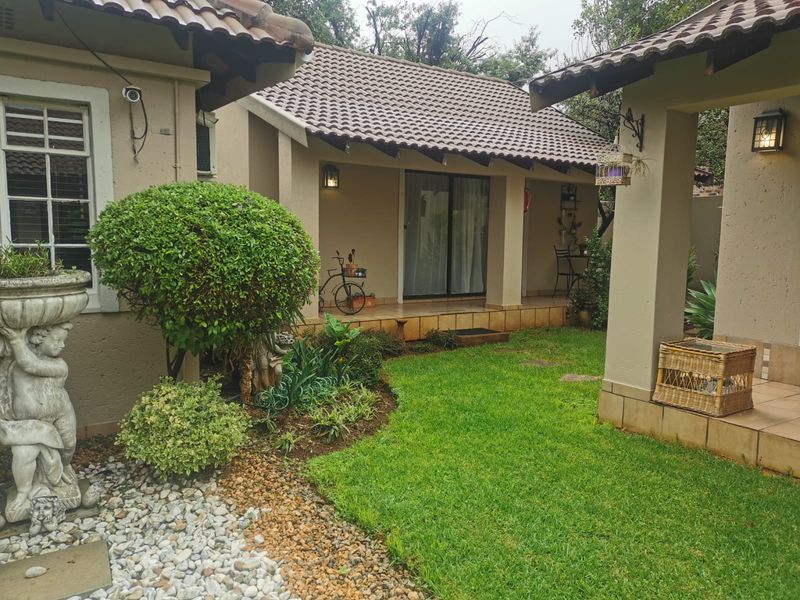 A well-maintained rear exterior view featuring a covered patio, tiled roof, and a landscaped garden area with established greenery.